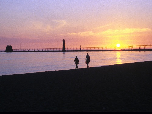 two people walking the beach at sunset, lighthouse in the distance