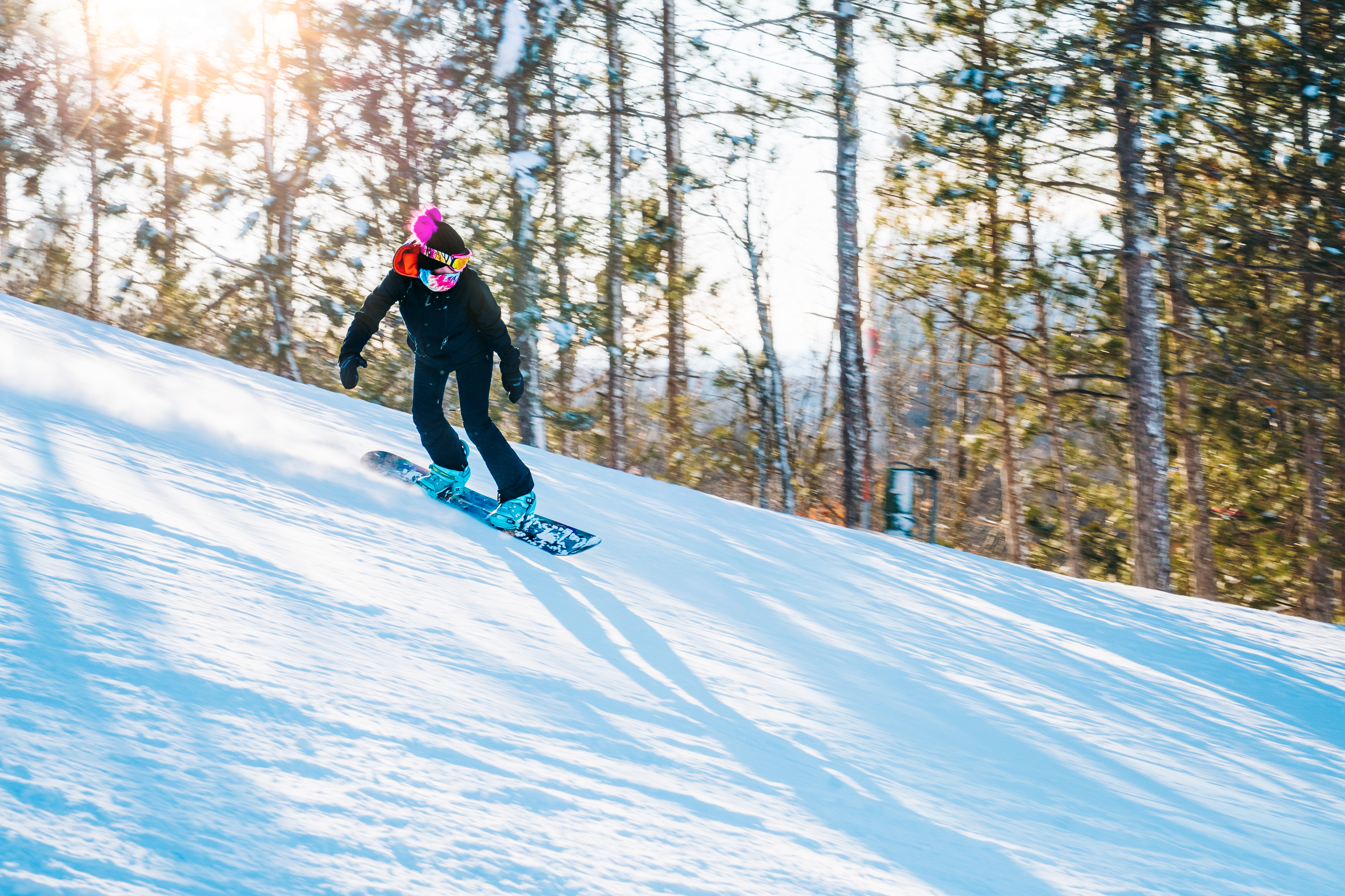 Snowboarder gliding down a ski hill by a tree line