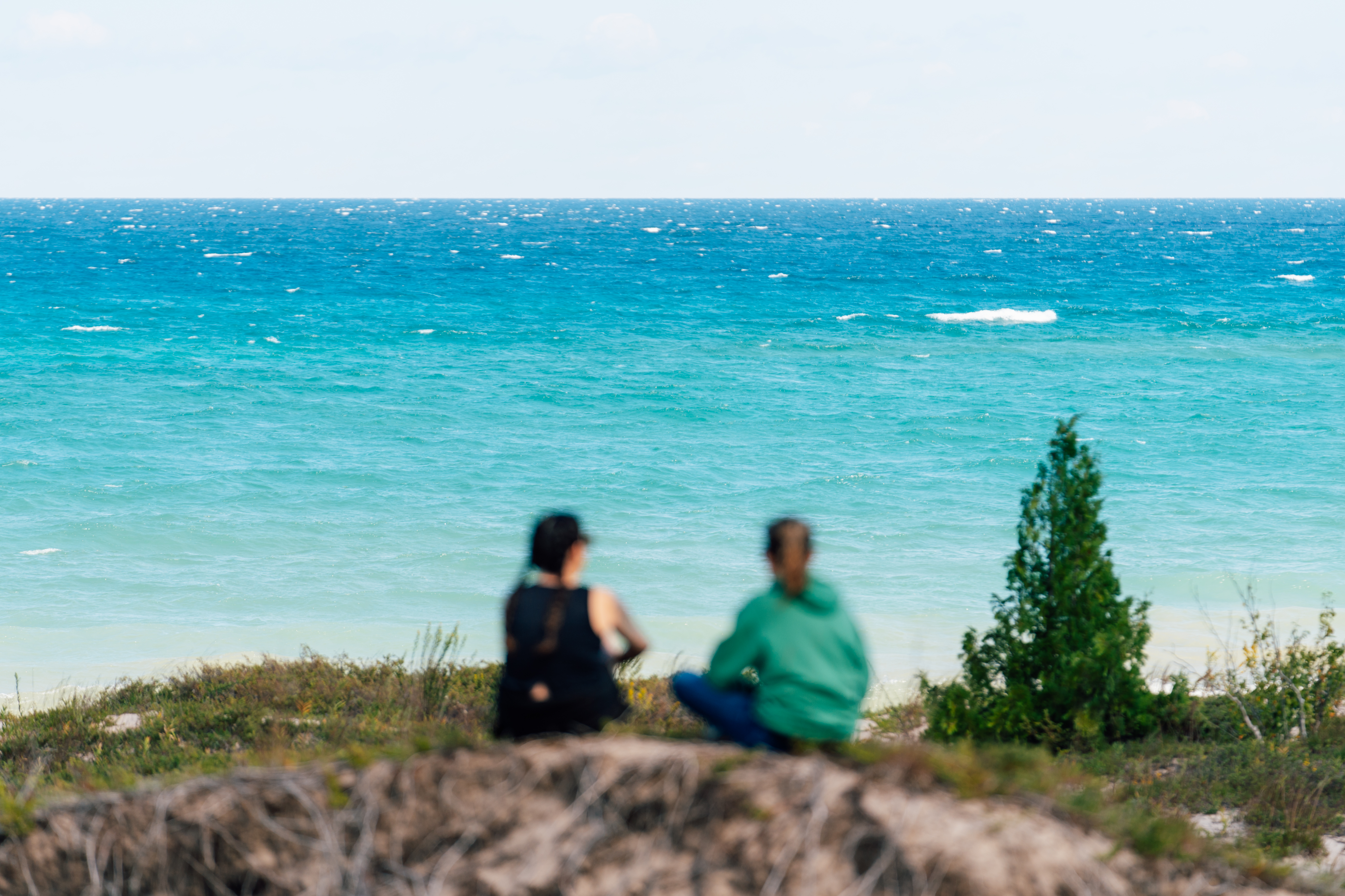 Two women sitting on a sand bluff near Lake Huron