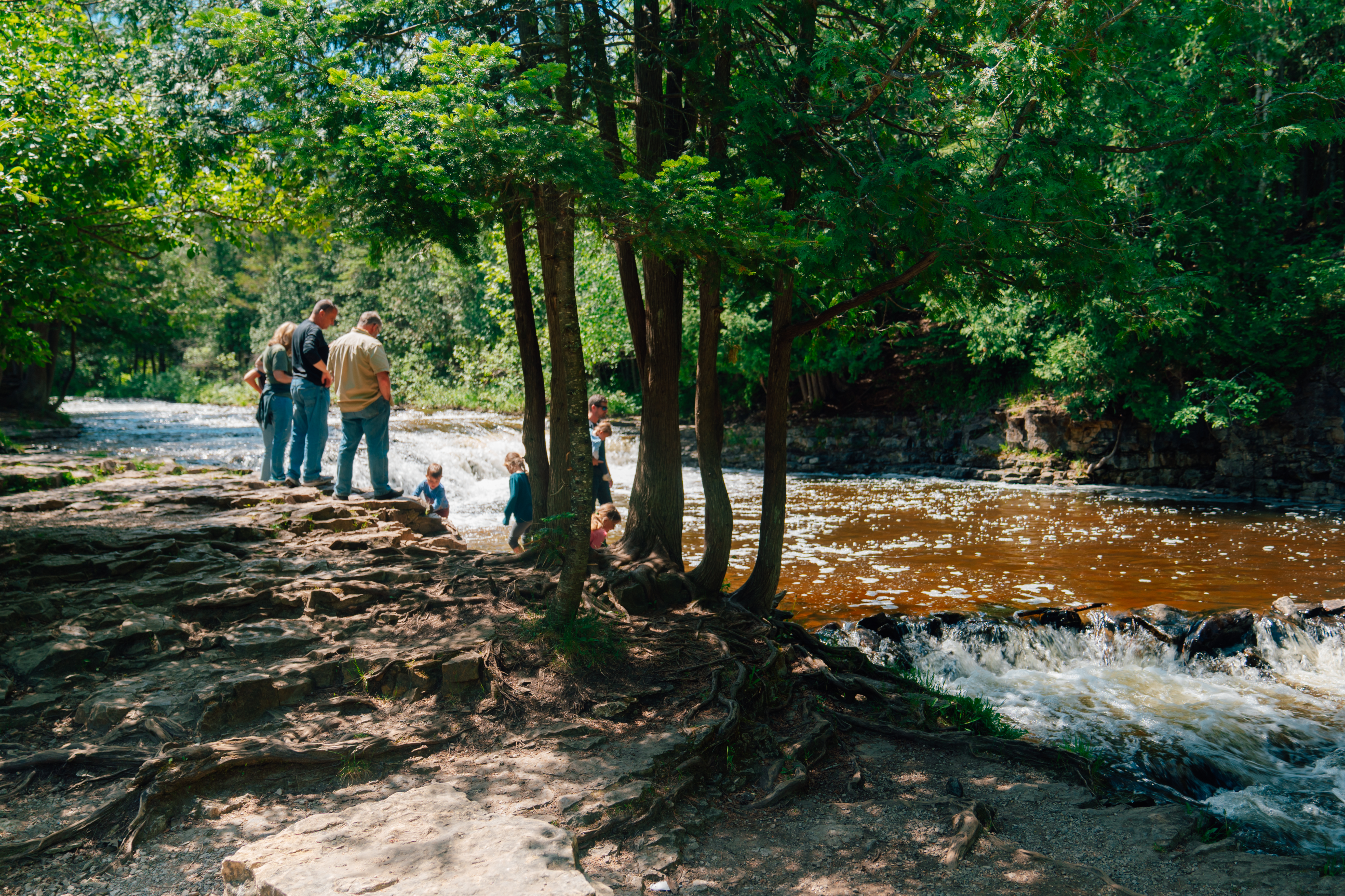 A family standing at the edge of the river near Ocqueoc Falls