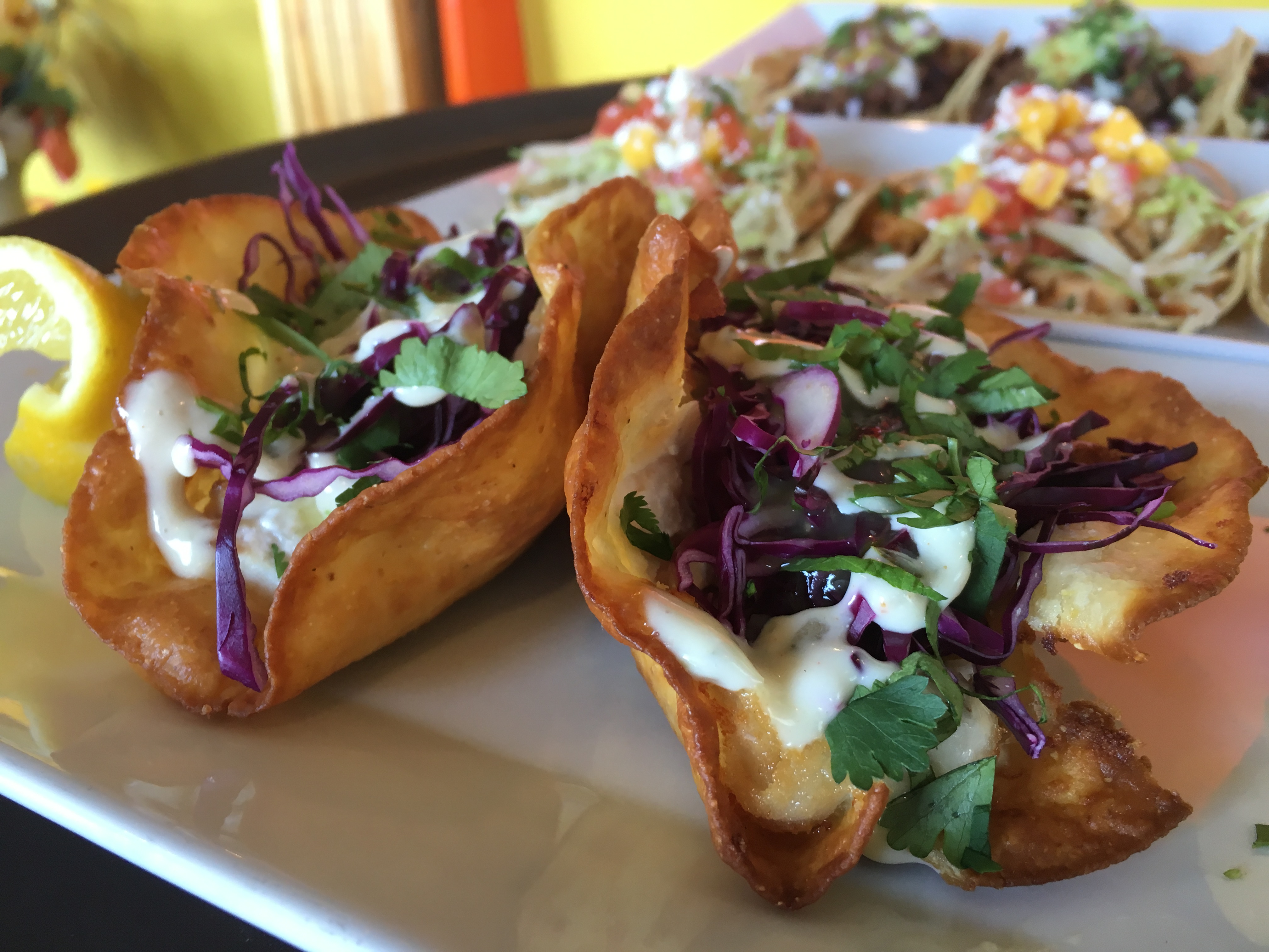Two fried fish tacos with a lemon wedge on the side