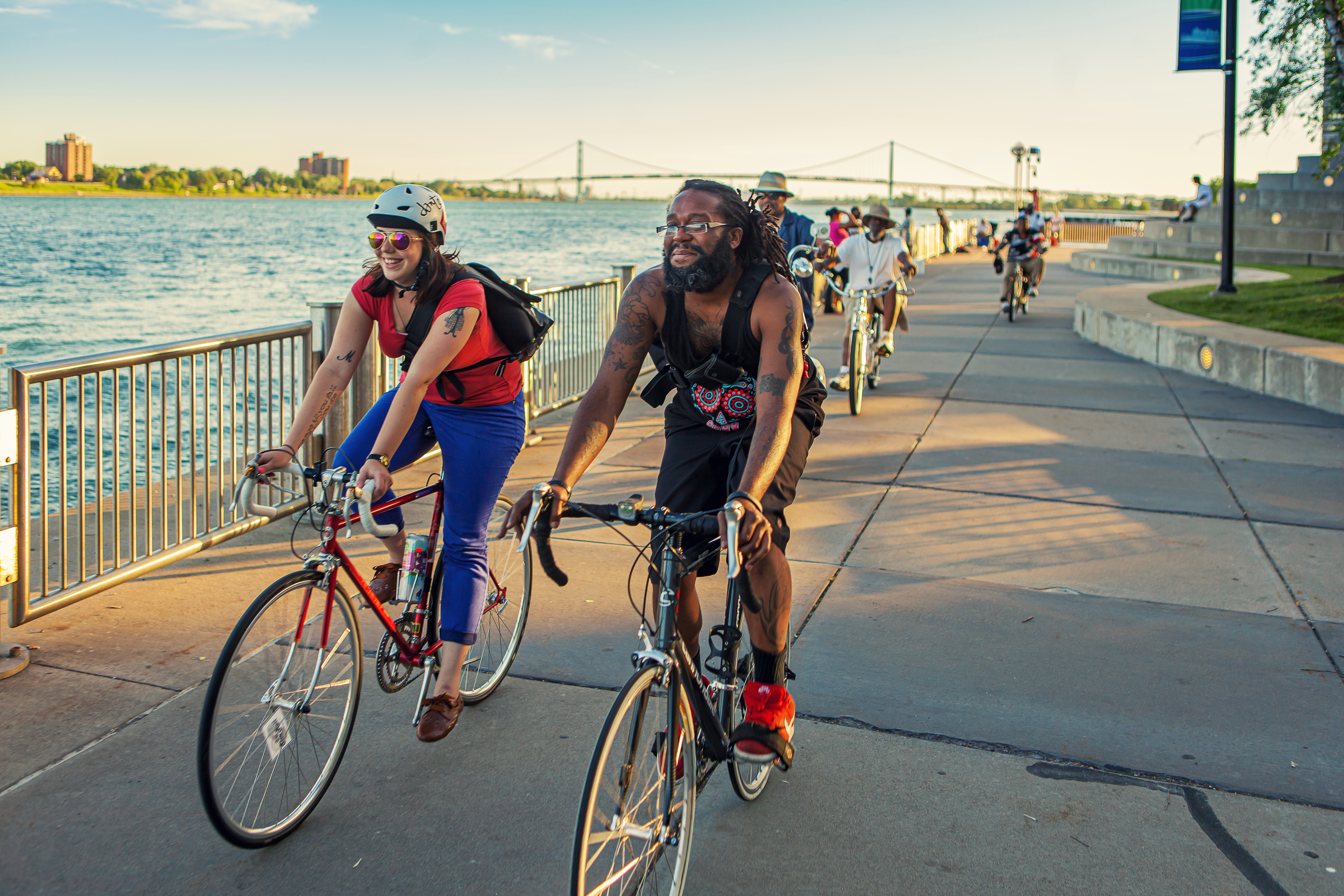 A man and woman biking on a paved path along the Detroit River