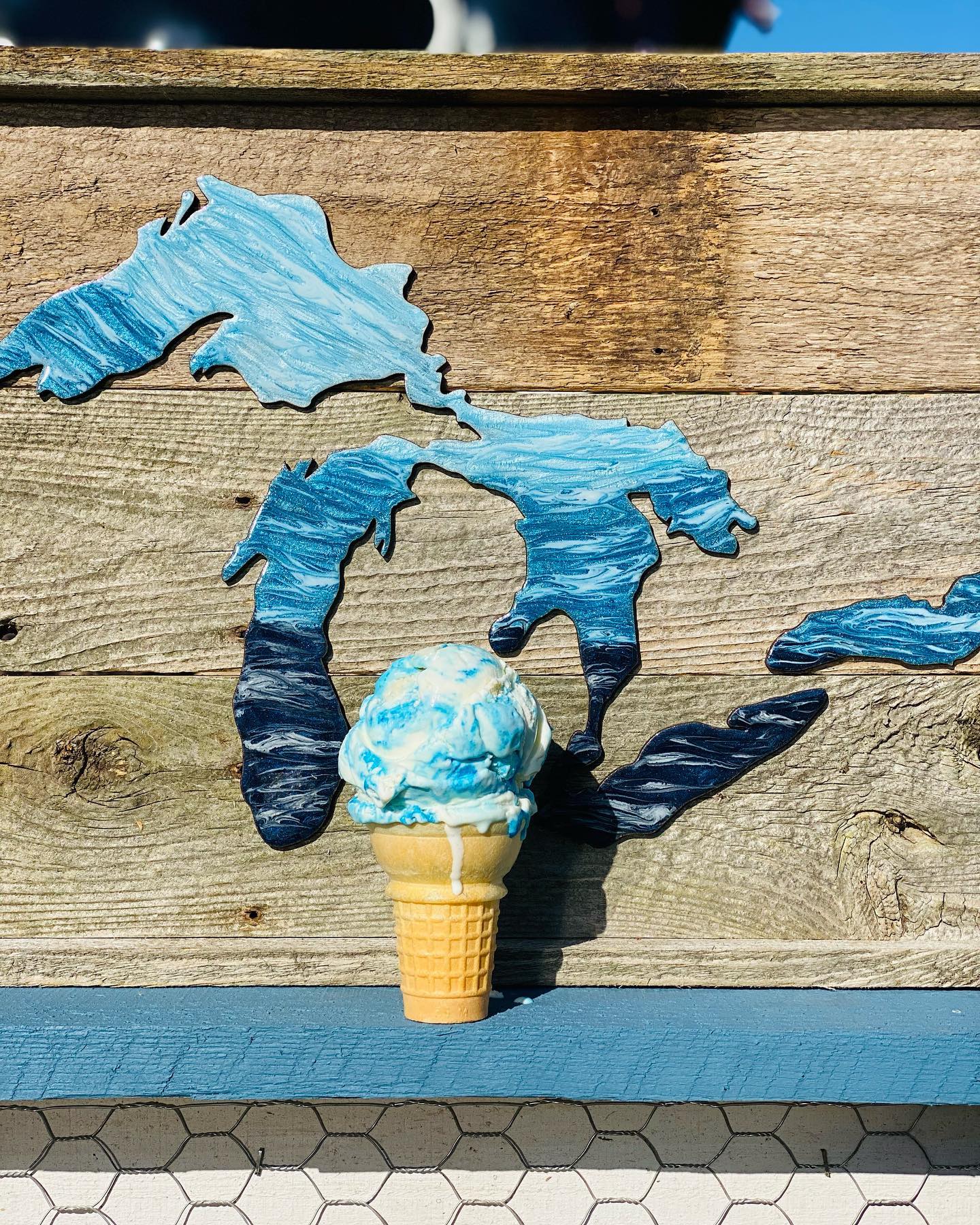MOO-ville Creamery A cone of ice cream in front of artwork of the Great Lakes.