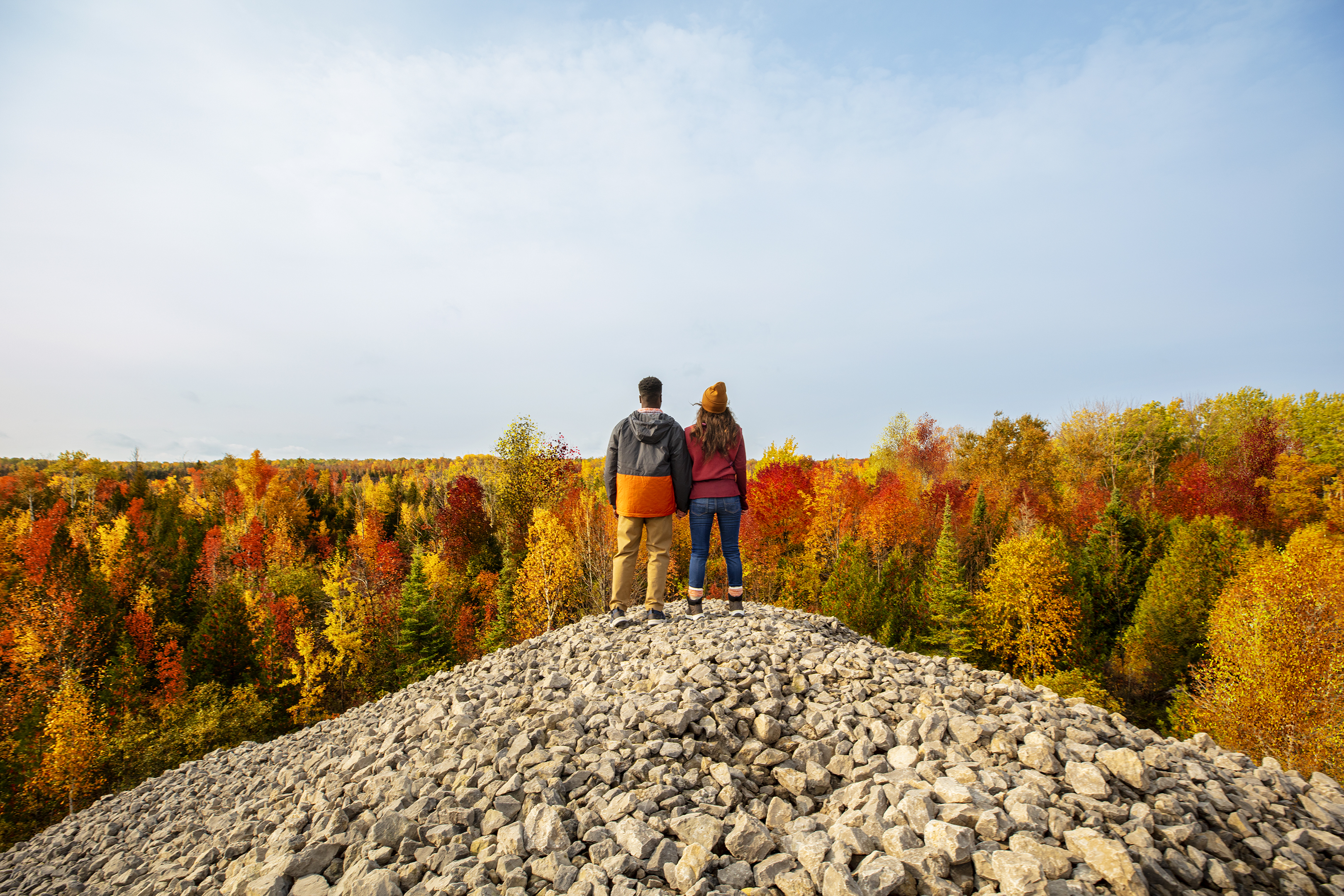A man and woman holding hands on a hill of rocks over a fall forest