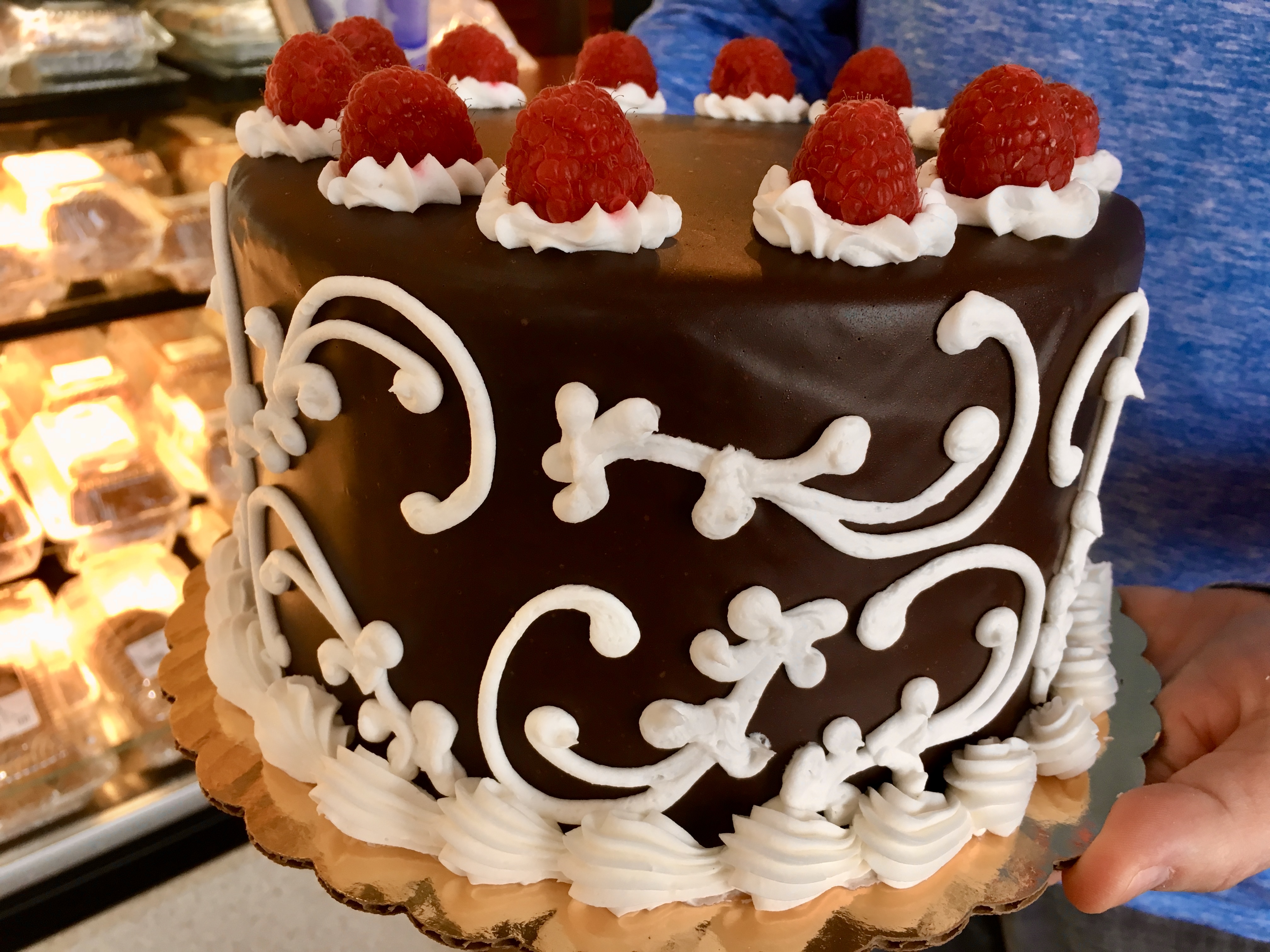 large chocolate tier cake with white icing swirls, raspberries on top and icing swirls on the bottom