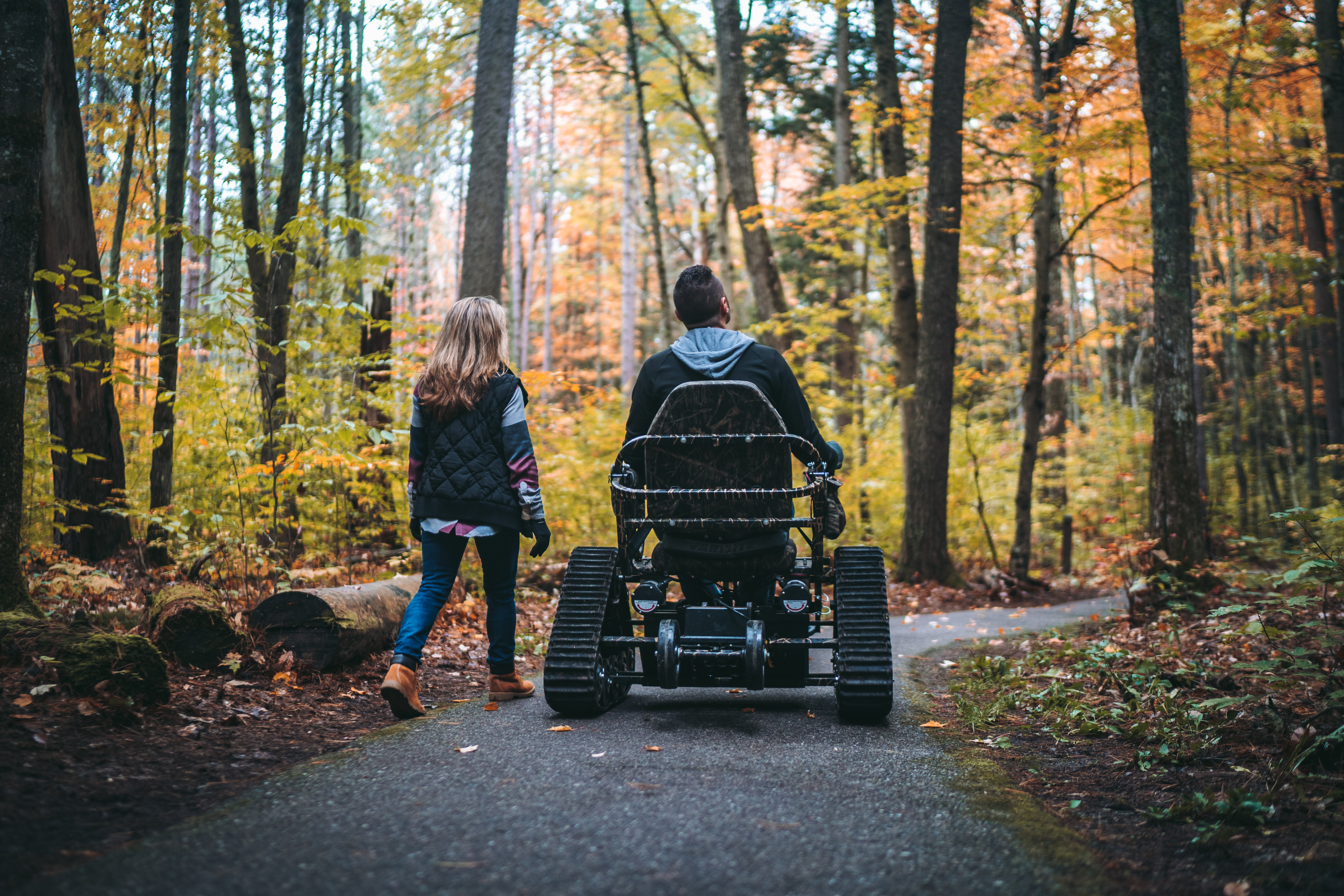 Accessibility at Hartwick Pines State Park A woman walking beside a man using a track chair on a trail