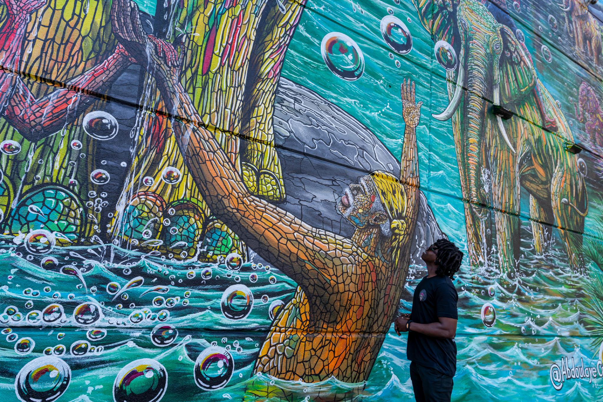 An artis standing beside their mural their mural. 