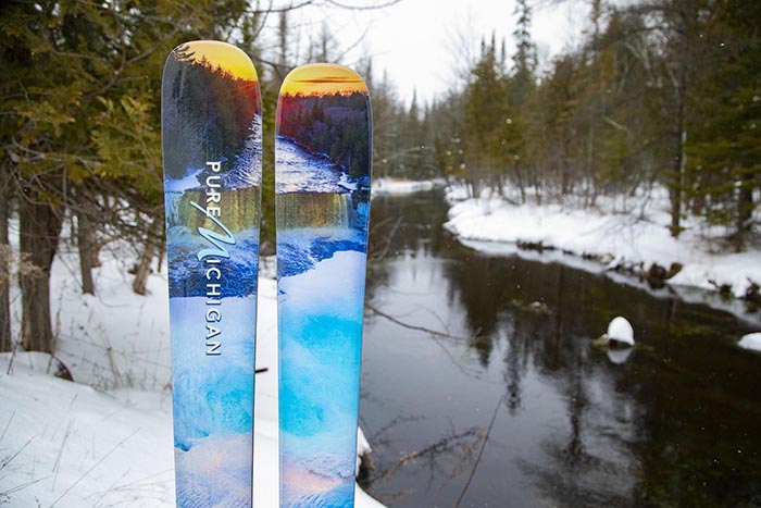 A pair of skis is standing up in the snow next to a river.
