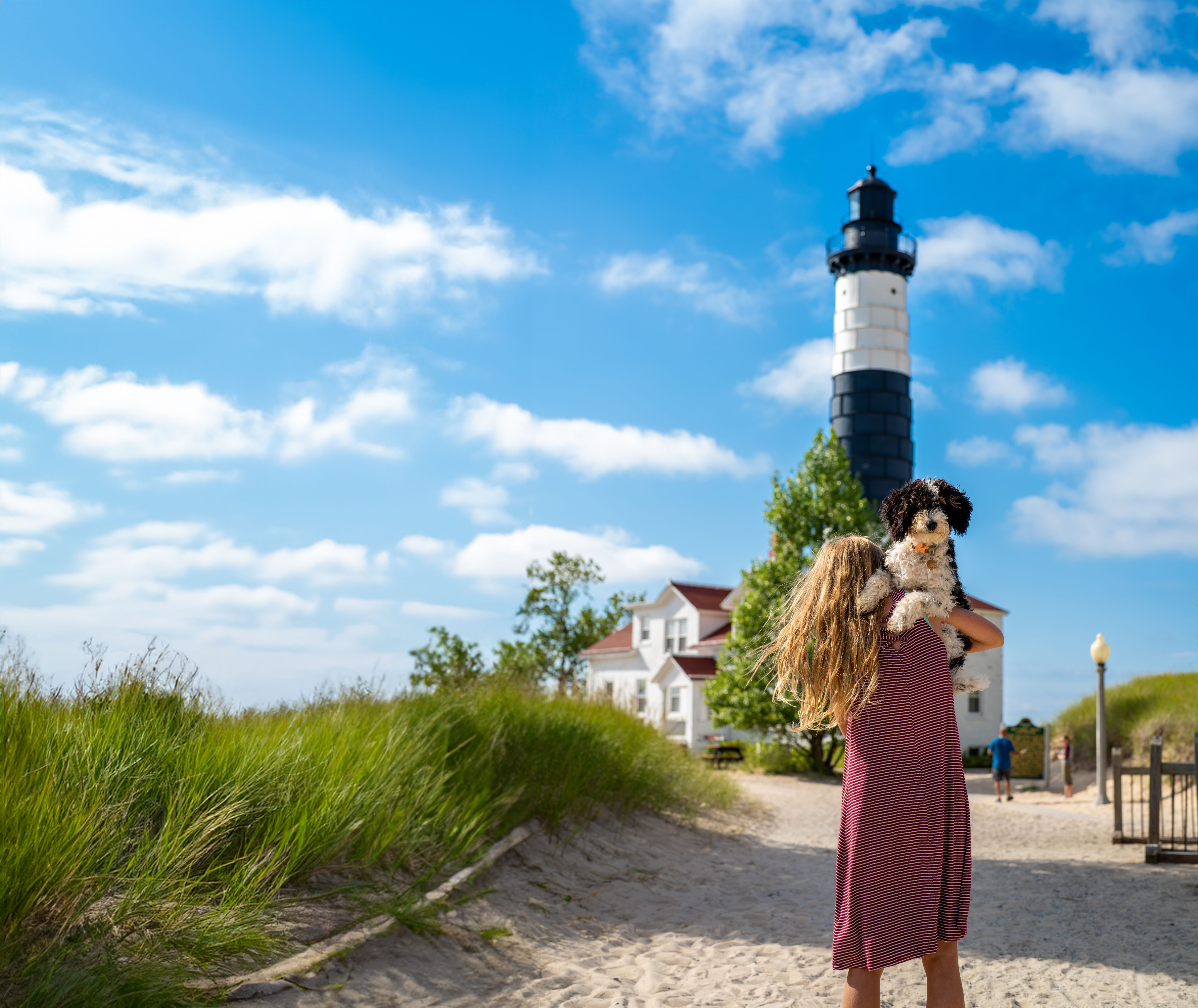 Ludington State Park A woman carrying a dog by a lighthouse and sea grass.
