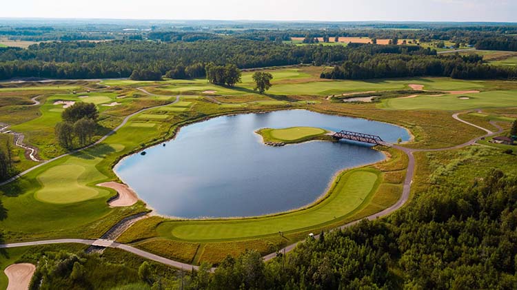 An aerial view of hole number 15 at Sweetgrass Golf Club. An isand green is surrounded by water within a small lake. 