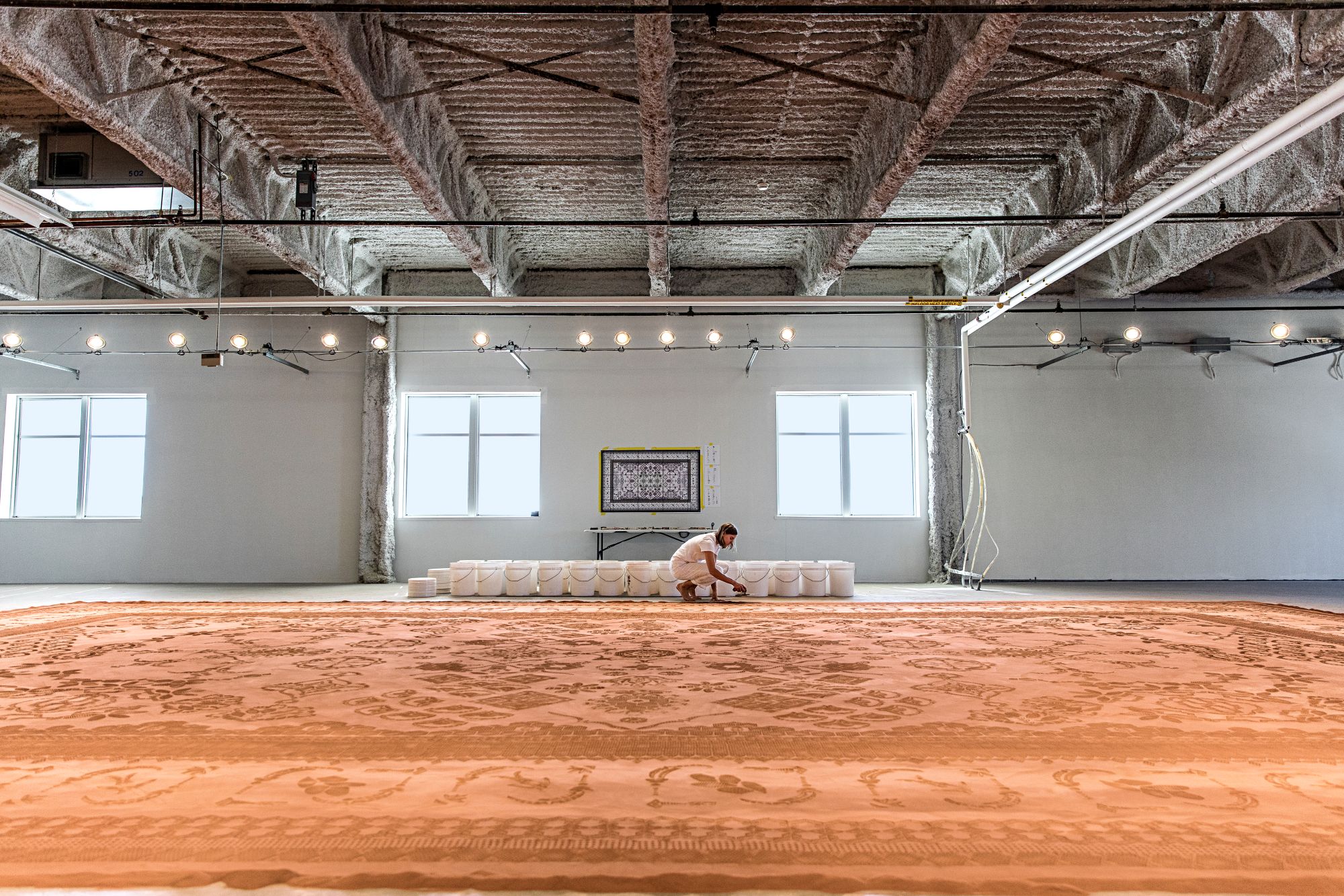 An artist creating a rug design out of dirt inside. 