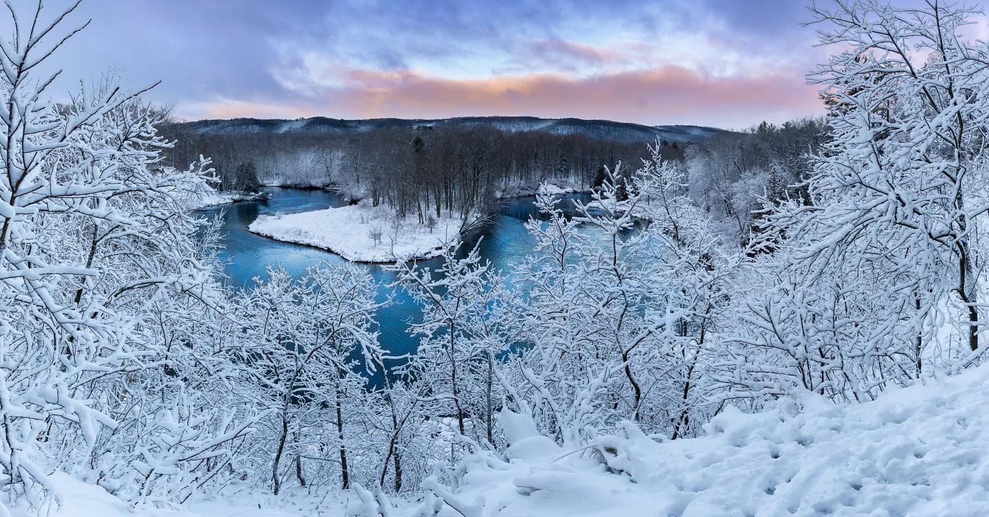 The Manistee River flowing through a forest covered with fresh snow. 