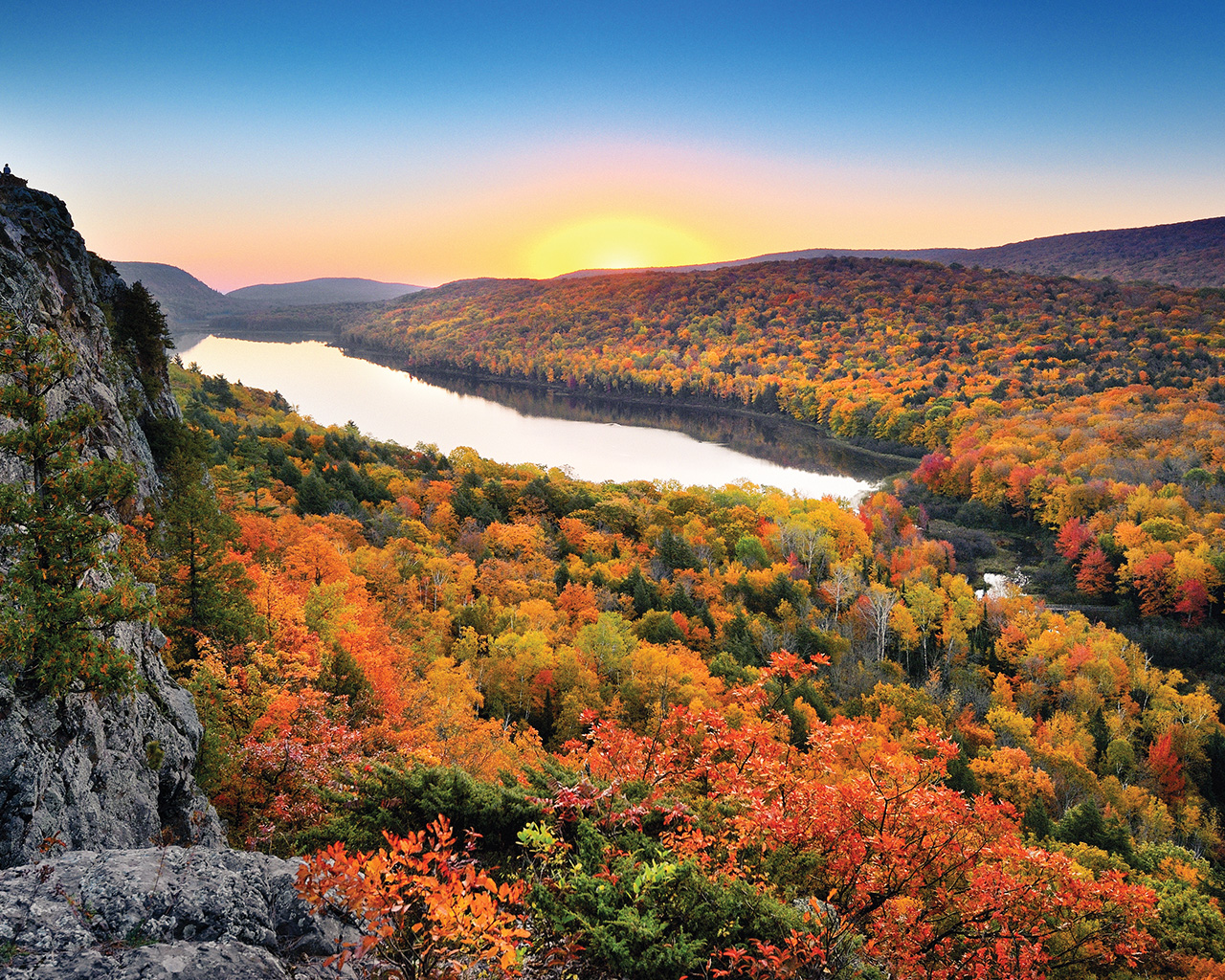 A lake in the mountains surrounded by fall trees at sunset. 