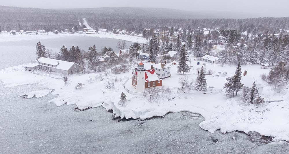 An aerial view of Eagle Harbor Lighthouse and the snowy coastline of Lake Superior in Michigan's Upper Peninsula 