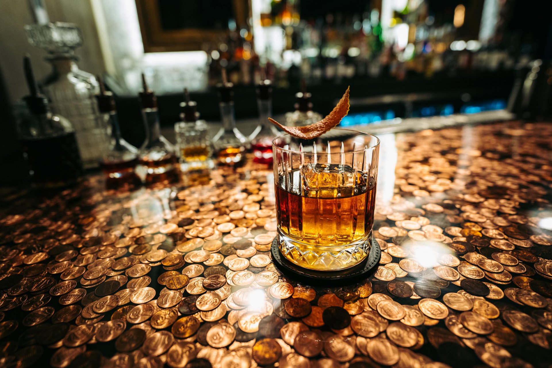 A cocktail with a dried orange rind on a bartop made of pennies. 
