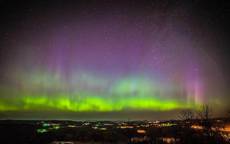 northern lights of purples, blues and greens, out over the water