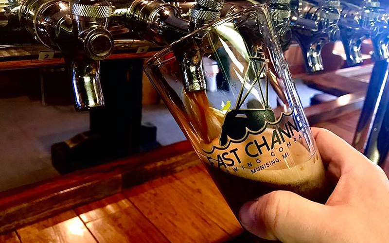 a glass of very dark craft beer being poured from the tap, logo on the glass