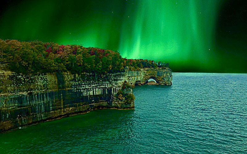 beautiful northern lights of green over pictured rocks and water is greenish blue