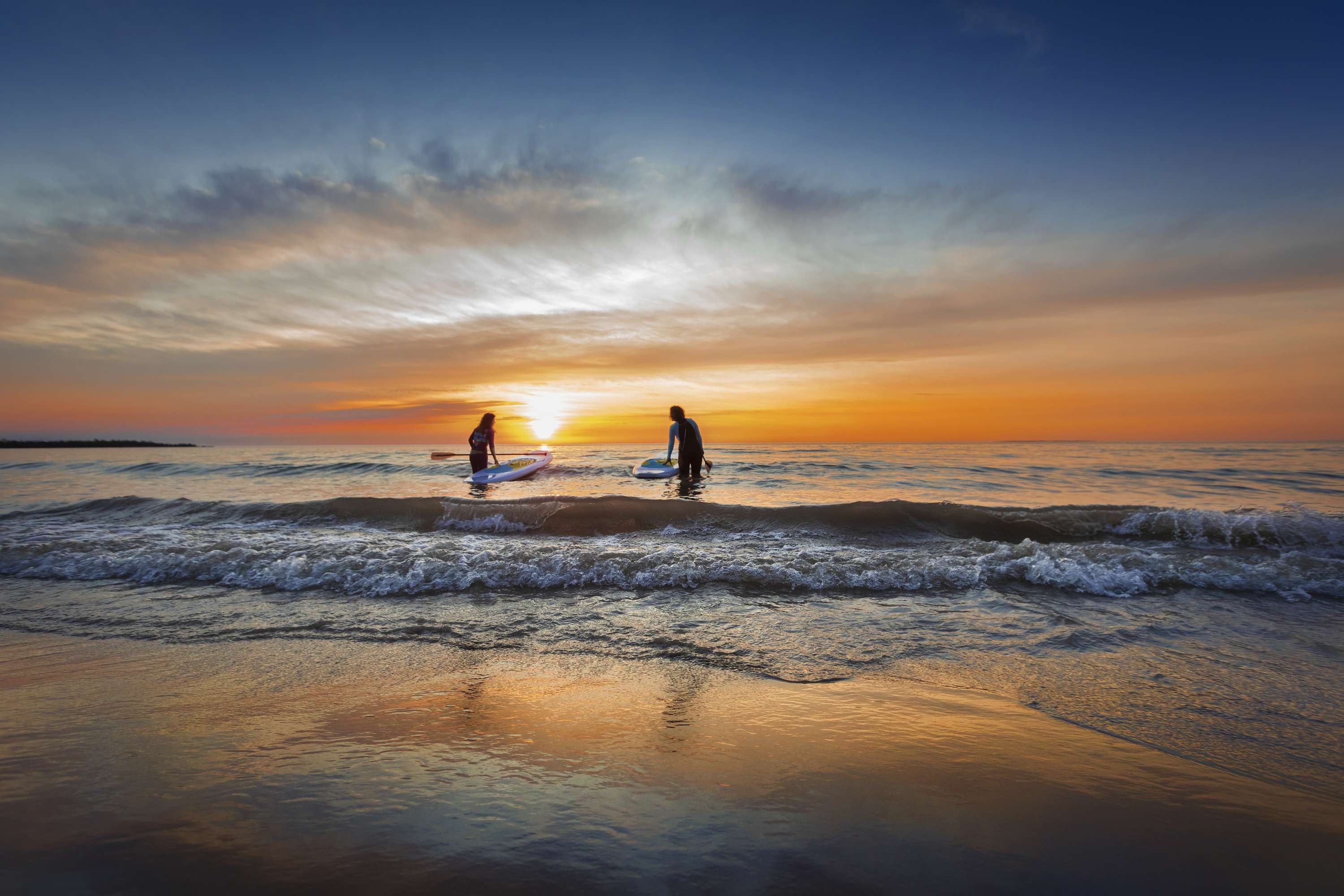 Two people in waves with paddle boards