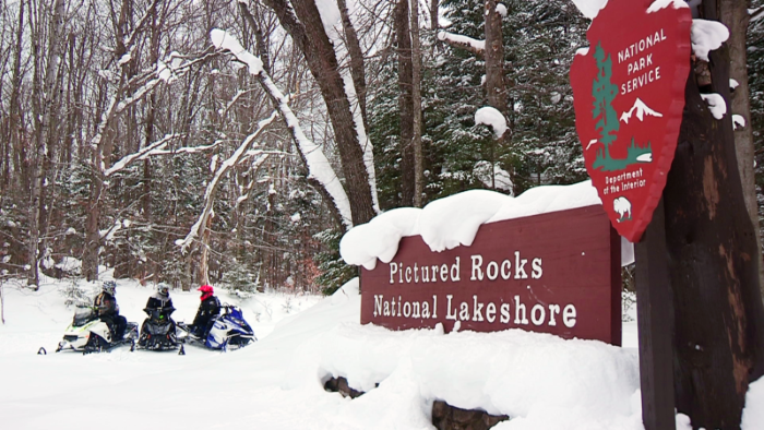 Group of snowmobilers resting by Pictured Rocks National Lakeshore sign