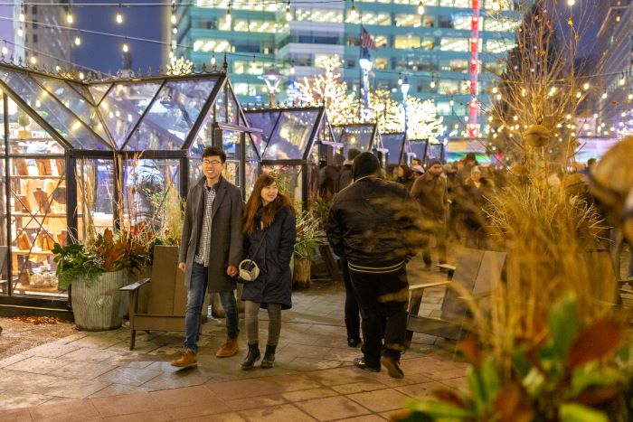 A couple waling in the glass house Christmas Village at night.