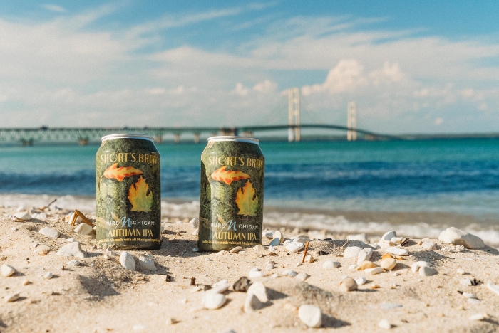 Two cans of Autumn IPA on the beach by the Mackinac Bridge