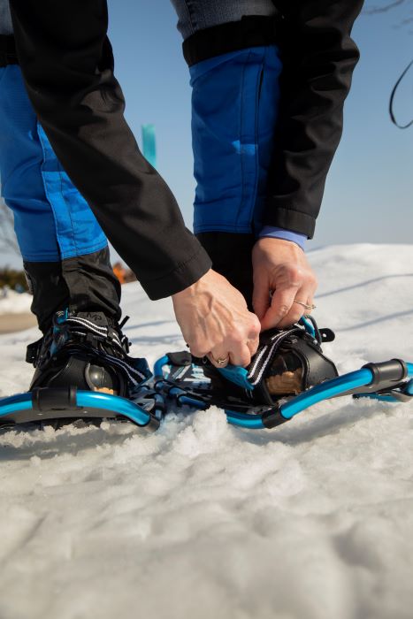 A person strapping snowshoes to their boots. 