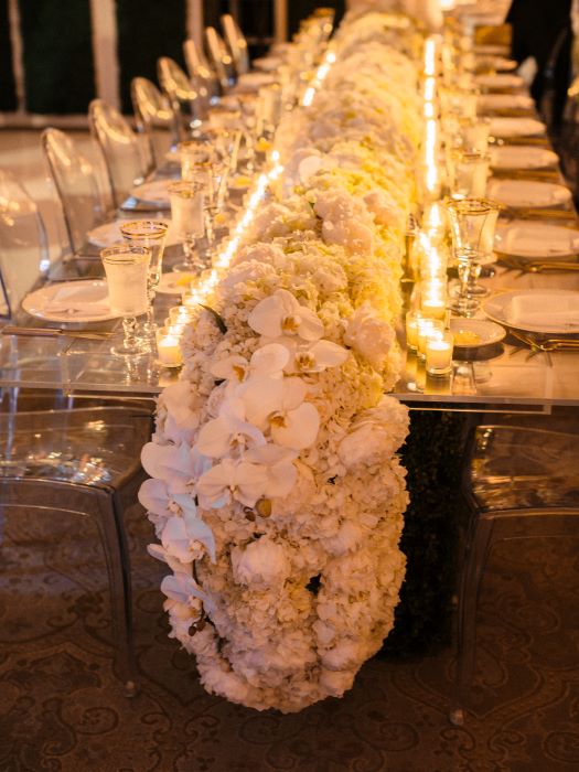 A table for guests decorated with a flower runner and candles.