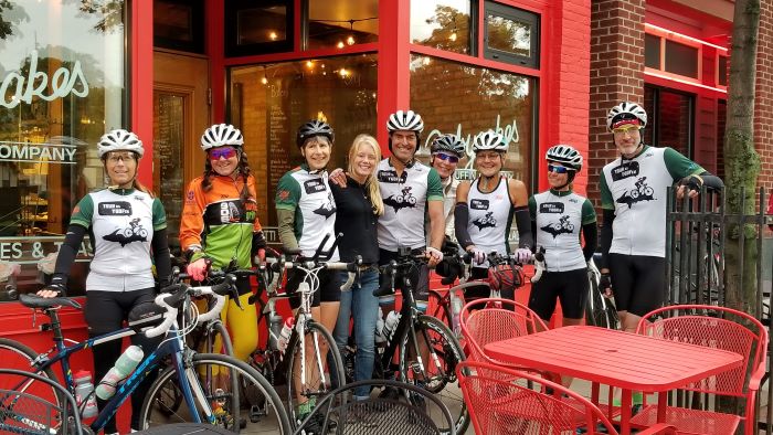 Bikers stand for group photo in front of Babycakes bakery with bikes