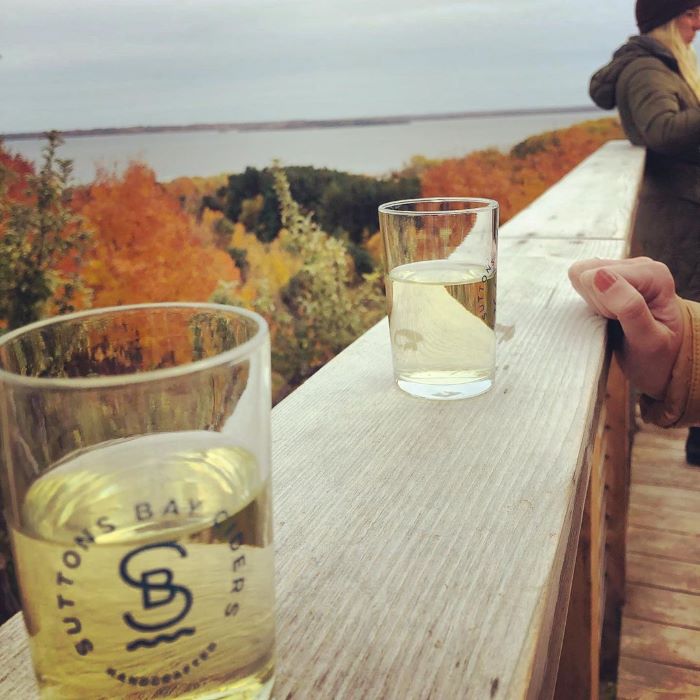 A glass of Suttons Bay Cider overlooking fall color trees