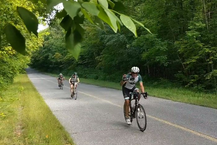 Road bikers ride down UP road surround by trees