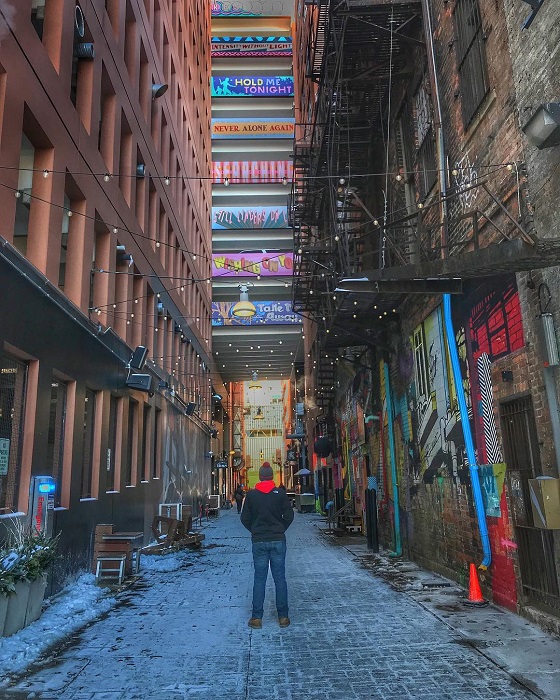 Traveler standing in alley painted with graffiti created by artists