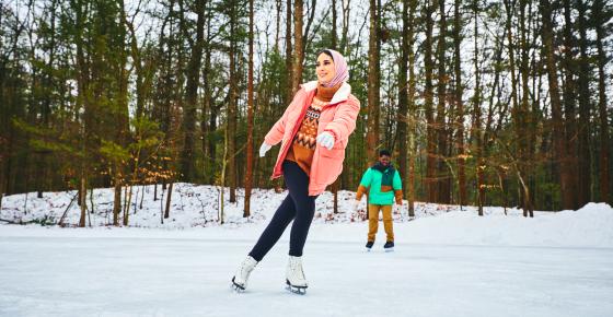 A woman ice skating outside near a forest