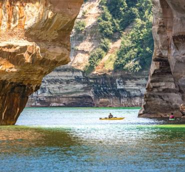 A kayaker paddling under a rock arch on Lake Superior