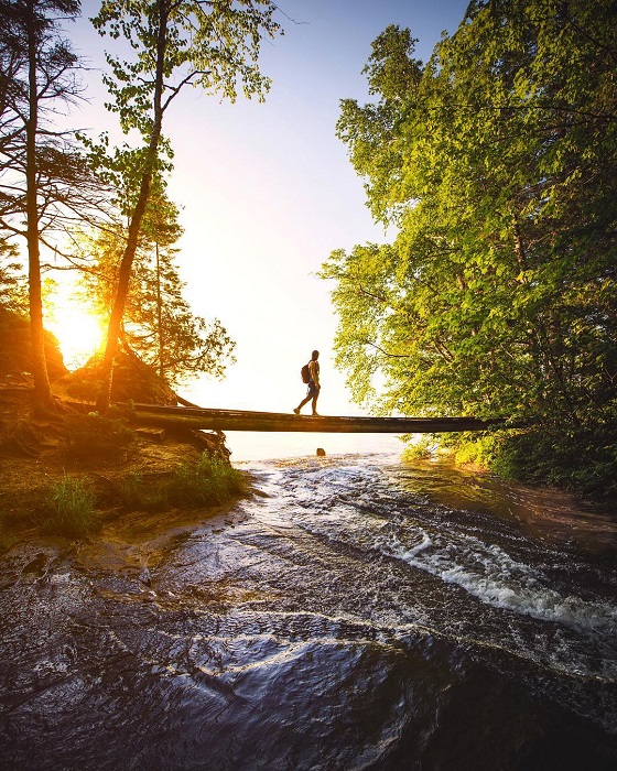 Backpacker hiking across bridge over river in the forest