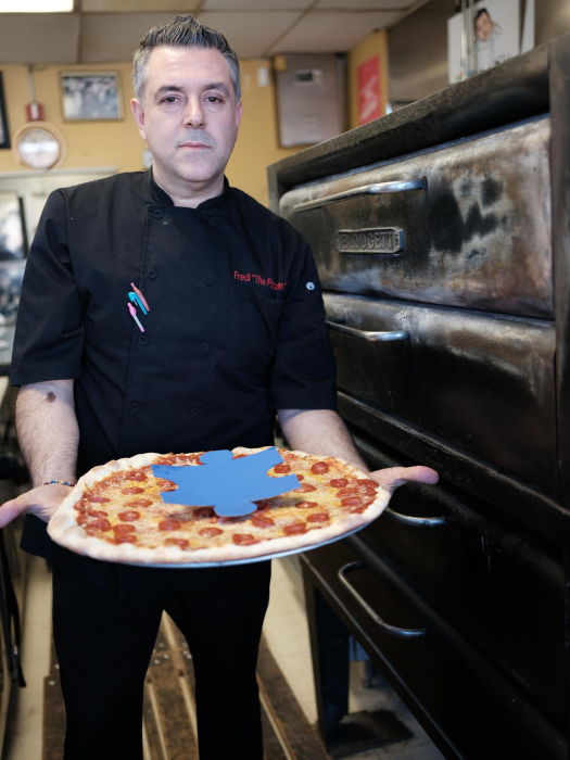 Fredi holding a fresh pepperoni pizza in the kitchen.