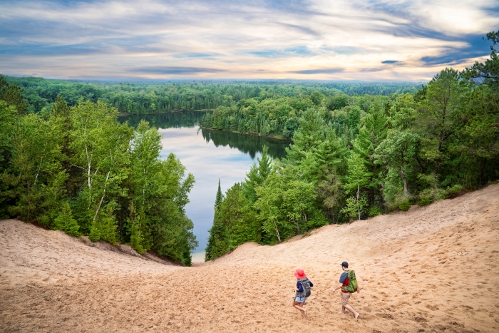 A man and woman walking down the Au Sable River dune surrounded by forest.