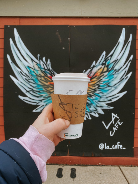 To-go coffee held in front of a mural.