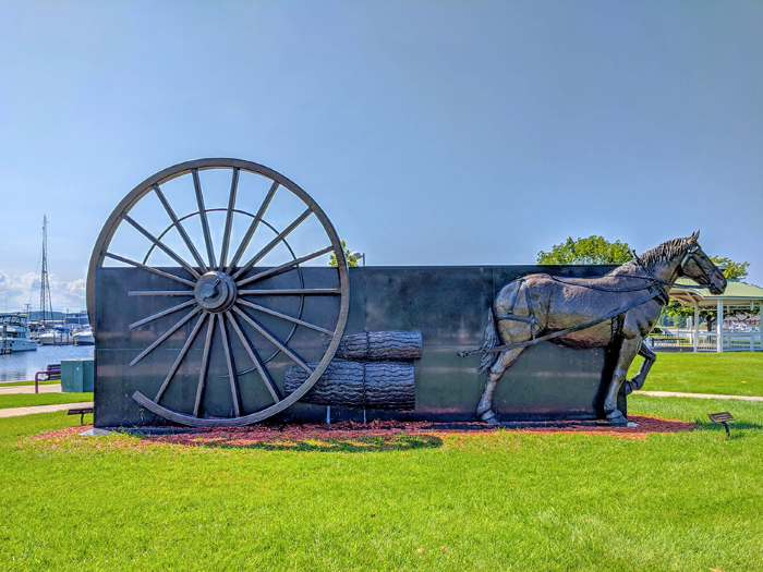 A sculpture of a horse pulling a lumber wagon.