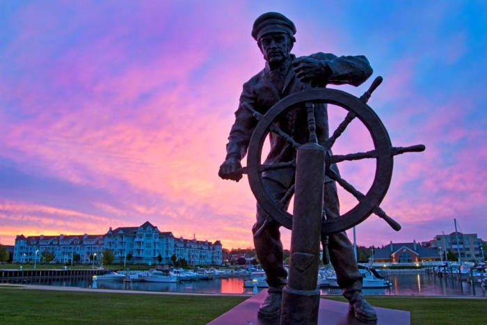 Sculpture of a captain at the wheel of a ship by a marina.